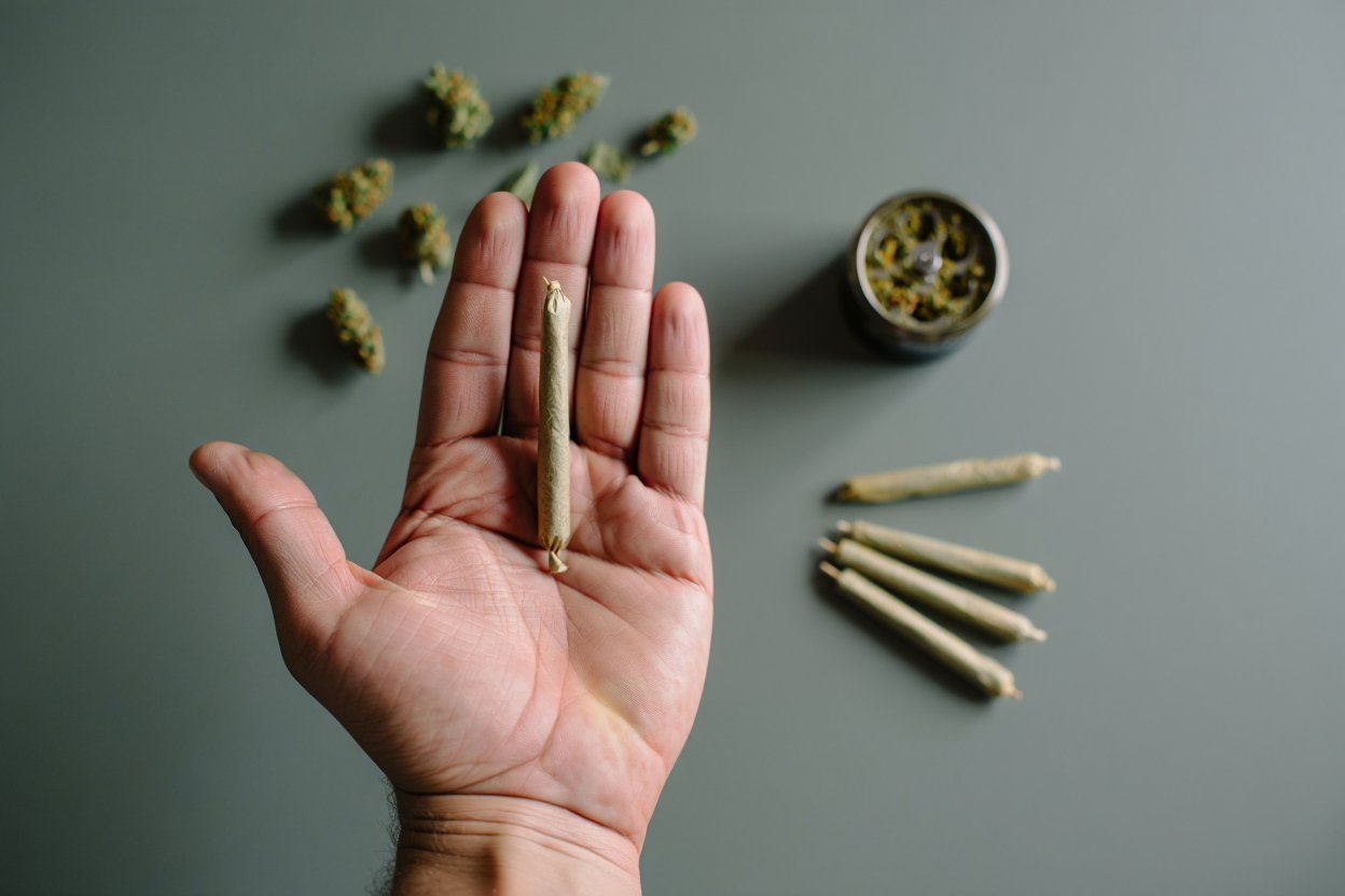 Рука держит джойнт на фоне марихуаны и гриндера